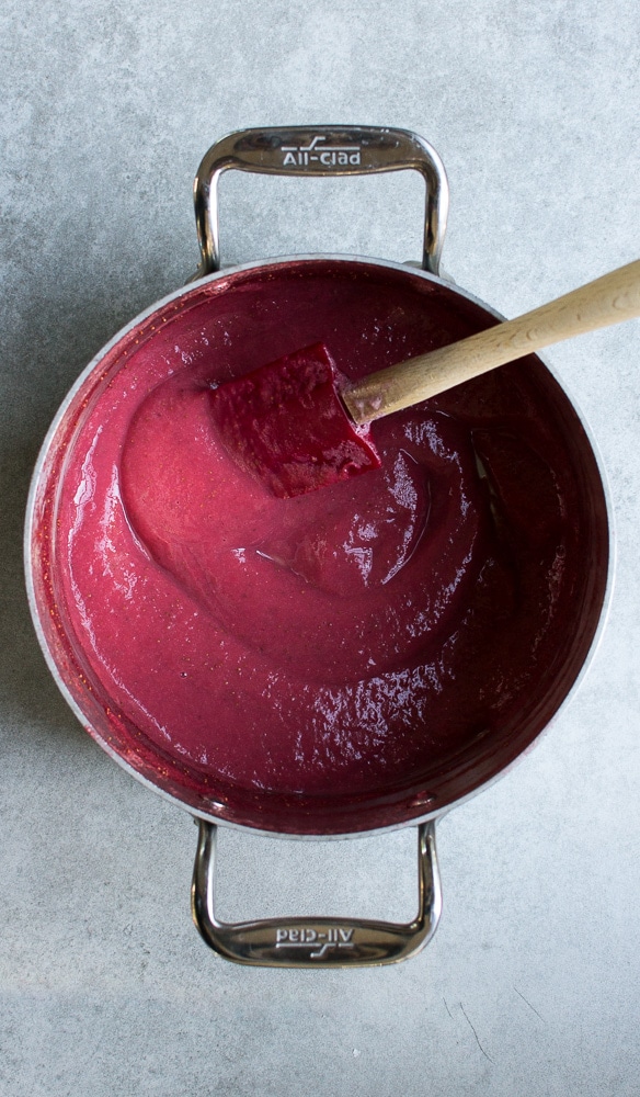 Vibrant pink and purple fruit-flavored candy melting in a stainless steel pot with a wooden spoon, ideal for homemade candy recipes.