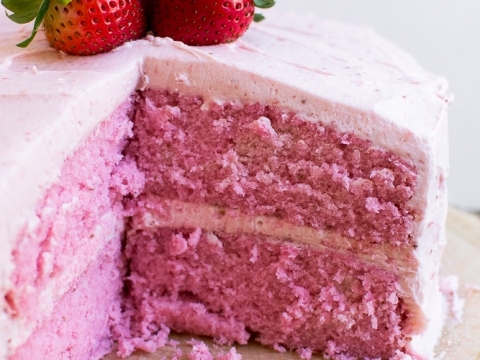 Fresh strawberry cake with pink frosting and strawberries on top.