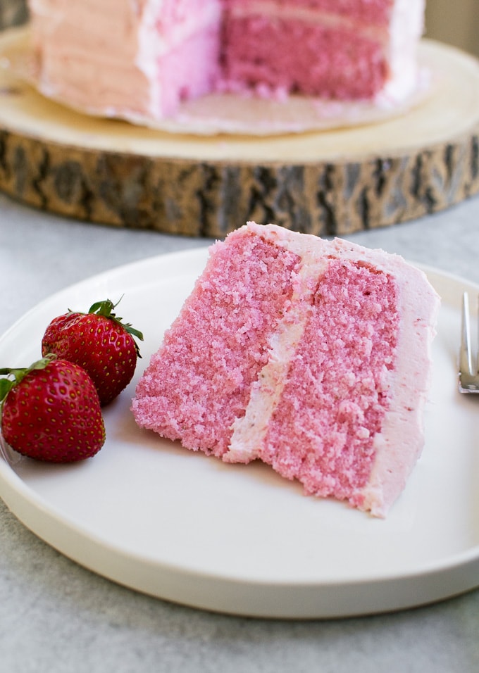 Sweet pink strawberry cake slice with fresh strawberries on white plate, delicious dessert from Stuck On Sweet.