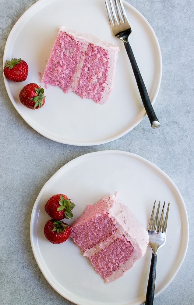 Strawberry cake slice on white plate with fresh strawberries and fork, top view.
