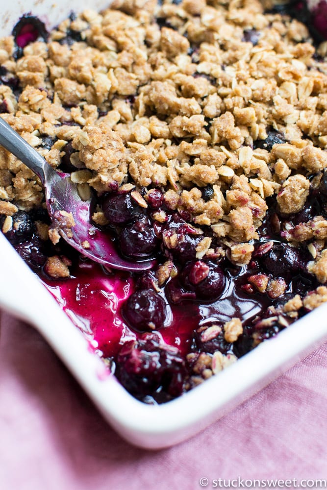 Freshly baked mixed berry crumble with a golden oat topping in a white baking dish.