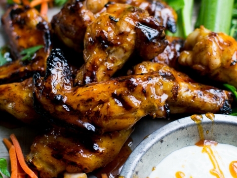 Juicy glazed chicken wings with side of fresh vegetables and dipping sauce, close-up of flavorful grilled chicken wings on a wooden platter with vibrant vegetables in the background.