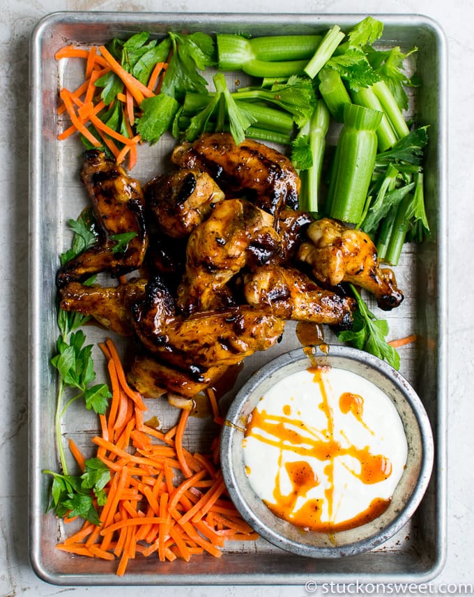 Juicy grilled chicken wings with fresh celery sticks, sliced carrots, and creamy dipping sauce on a metal tray. Perfect for snacks, appetizers, or a delicious meal.