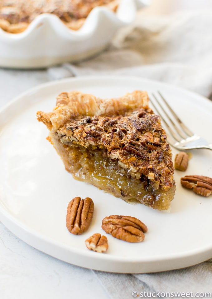 Sweet homemade pecan pie slice on a white plate with pecans around it, showcasing a golden flaky crust and gooey filling. Perfect for dessert or holiday gatherings.