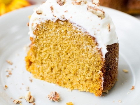 Pumpkin bundt cake with cream cheese frosting and chopped nuts on top, served on a white plate.