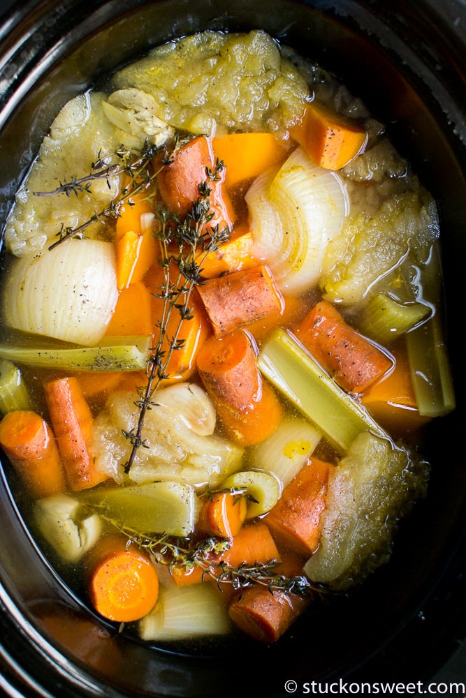 Fresh vegetables and herbs in a slow cooker for healthy vegetable broth or stew, featuring carrots, celery, onions, and thyme. Perfect for homemade, comforting, nutritious meals.