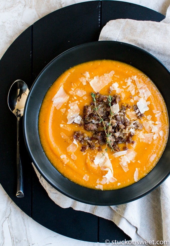 Creamy butternut squash soup garnished with crumbled cheese and fresh thyme, served in a black bowl on a rustic table, perfect for cozy comfort food.