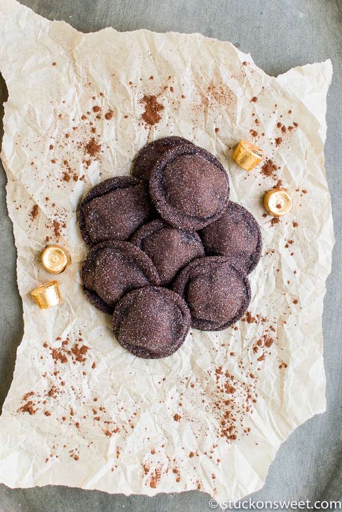 Rich chocolate cookies with a dusting of cocoa powder on crumpled parchment paper, surrounded by caramel candies, perfect for dessert lovers.