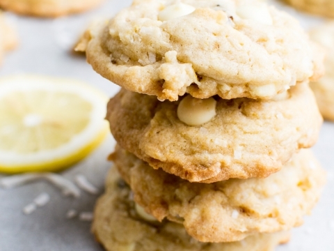 Buttery lemon sweet cookies with white chocolate chips stacked with lemon wedges on background.