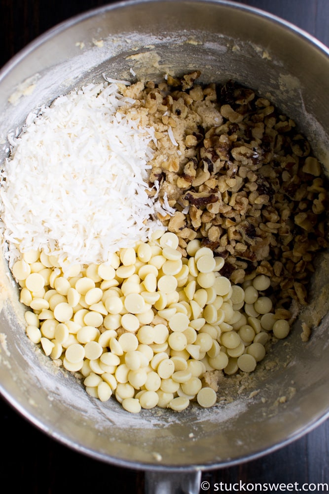 Cream cheese, chopped white chocolate, shredded coconut, and chopped nuts in mixing bowl for cookie dough recipe.
