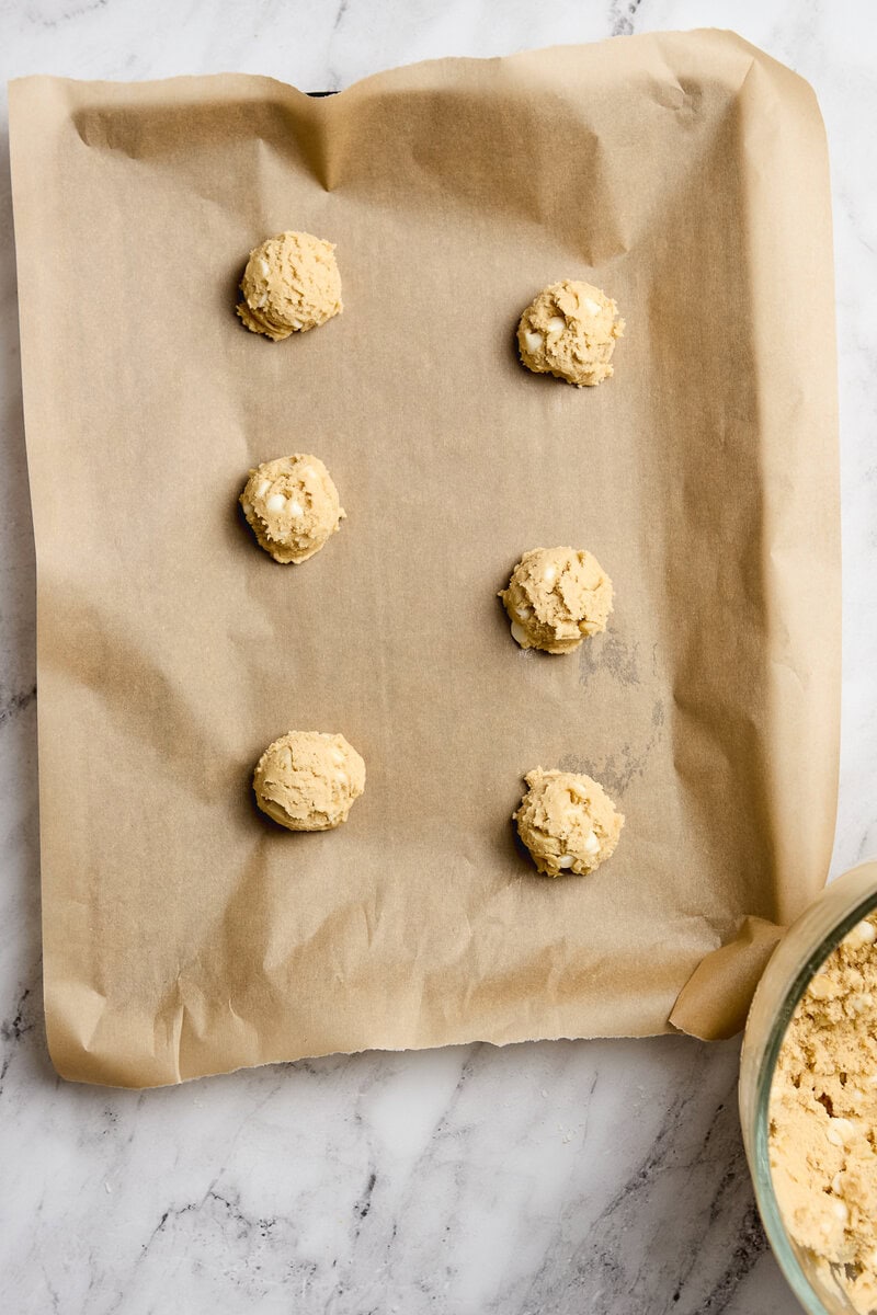 Creamy cookie dough balls on parchment paper with a bowl of cookie dough in the corner, perfect for baking or snacking. Ideal for homemade cookie recipes and sweet treat ideas.