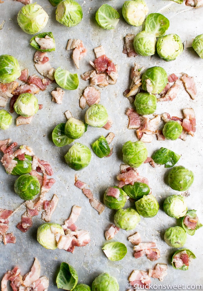 Fresh Brussels sprouts with diced bacon on baking sheet, ready for roasting, top view.