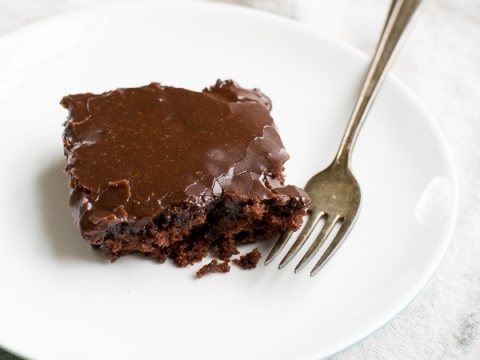 Decadent chocolate brownie with rich, glossy ganache topping on a white plate with a silver fork, perfect for satisfying sweet tooth cravings.