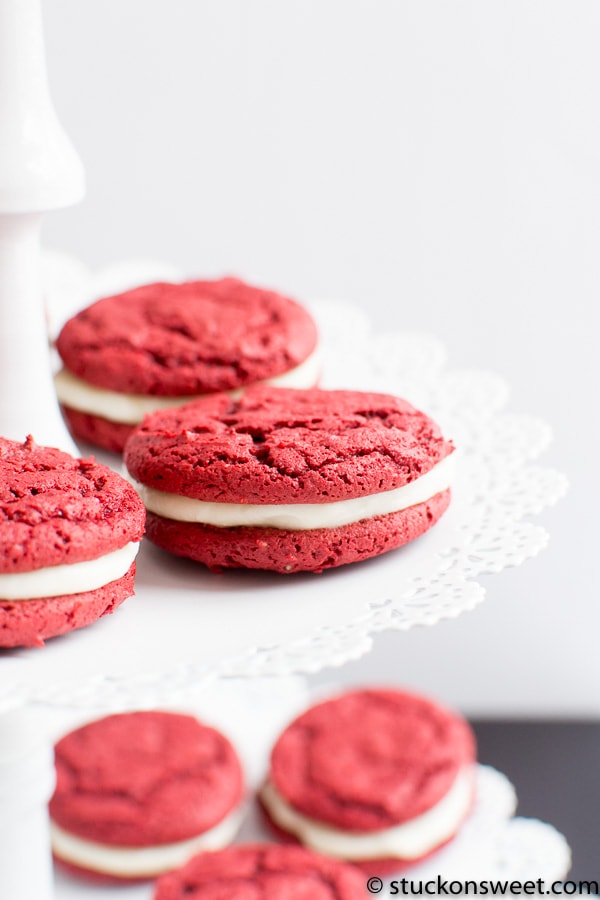 Red cookies with vanilla cream filling on a white stand, perfect for sweet treats and dessert lovers.
