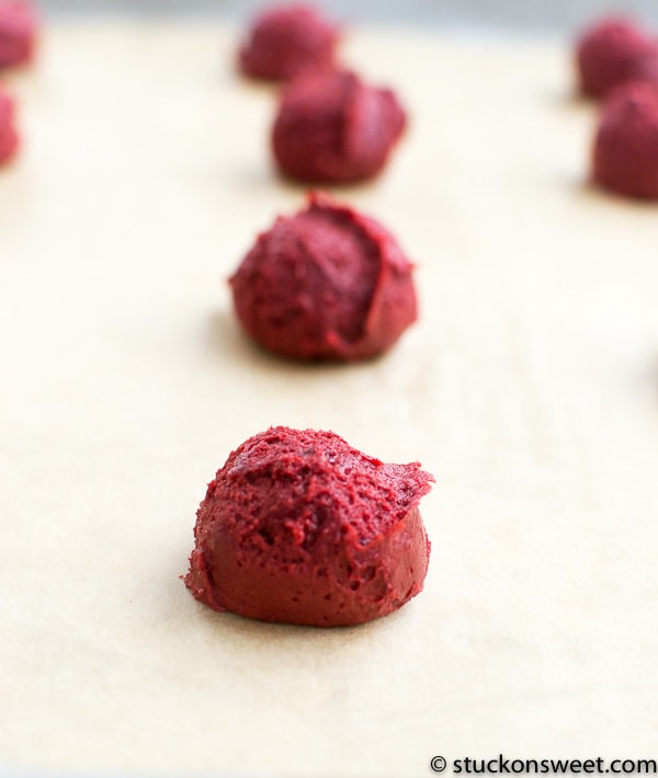 Fresh red velvet cookie dough balls on parchment paper, ready to bake, showcasing homemade sweet treats from Stuck On Sweet.