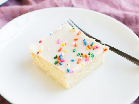 Bright white birthday cake with colorful sprinkles on top, served on a white plate with a fork, perfect for celebrations.