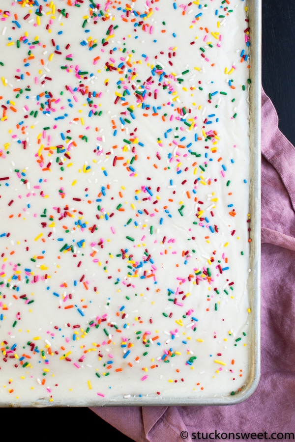 Colorful sprinkle-topped vanilla cake with white frosting in a metal baking pan, perfect for celebrations and dessert cravings.