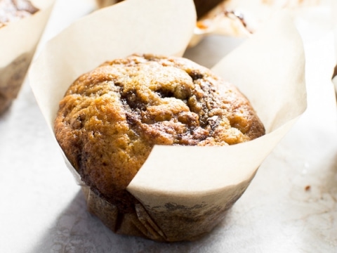 Rich chocolate chip muffin in parchment paper liner, fresh baked and golden brown, perfect for breakfast or snack.