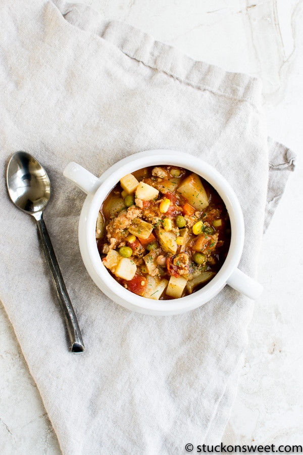 Comforting homemade vegetable beef stew in a white mug with a spoon, served on a rustic linen cloth, perfect for cozy home-cooked meals.
