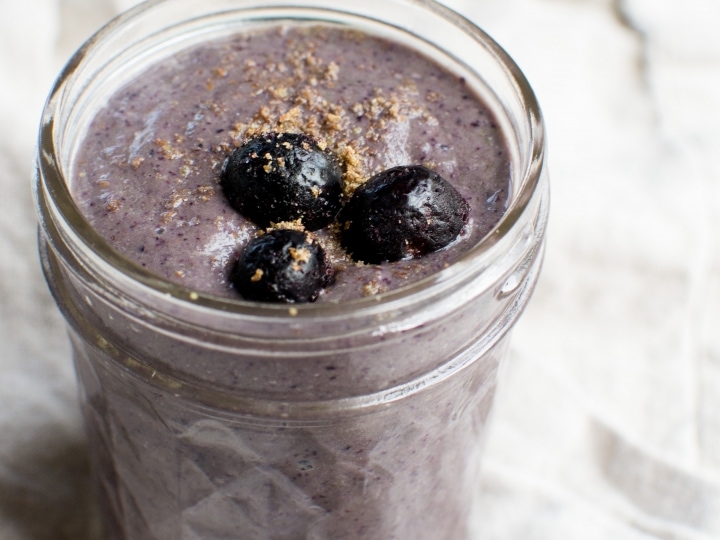 Creamy blueberry smoothie in a glass jar, topped with whole blueberries and a sprinkle of crushed graham crackers, perfect for breakfast or a healthy snack.