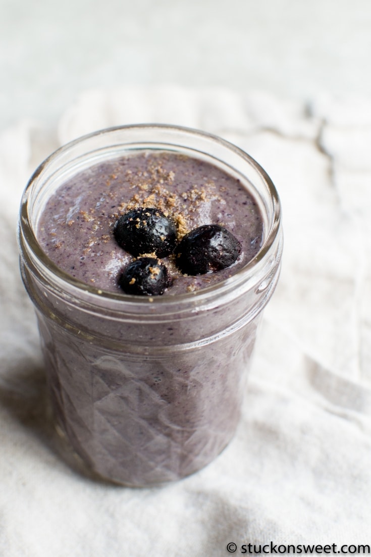 Creamy blueberry smoothie in a glass jar, topped with whole blueberries and a sprinkle of crushed graham crackers, perfect for breakfast or a healthy snack.