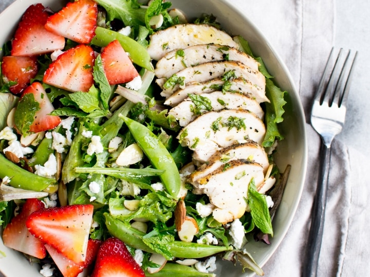 Fresh chicken salad with strawberries, greens, almonds, and feta cheese in a white bowl ready to serve.