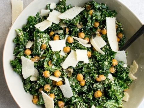 Creamy kale salad with chickpeas and shaved Parmesan cheese in a white bowl on gray background. Perfect for healthy meals and vegetarian lunch ideas.