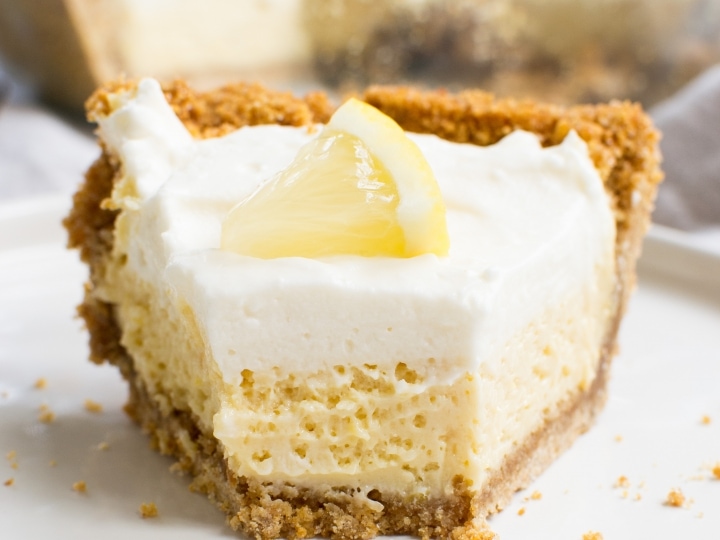 Rich homemade lemon cheesecake with a buttery graham cracker crust, topped with whipped cream and lemon slice, perfect for dessert lovers and lemon dessert enthusiasts.