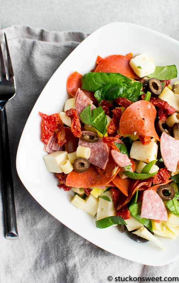 Crispy Italian antipasto salad with fresh mozzarella, black olives, cured meats, and mixed greens on a white plate. Perfect for a light, savory appetizer or meal.