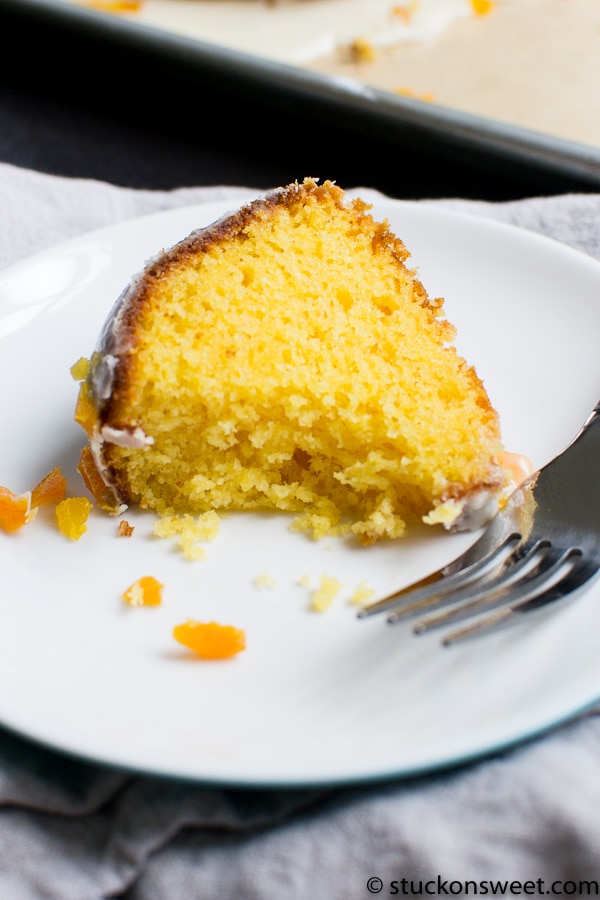 Fluffy yellow cake slice with moist interior and frosting on a white plate, with crumbs and a fork, perfect for dessert or teatime.