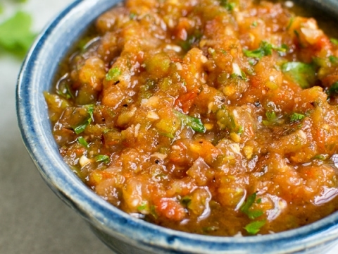 Spicy homemade salsa with tomatoes, onions, and cilantro in a blue ceramic bowl.