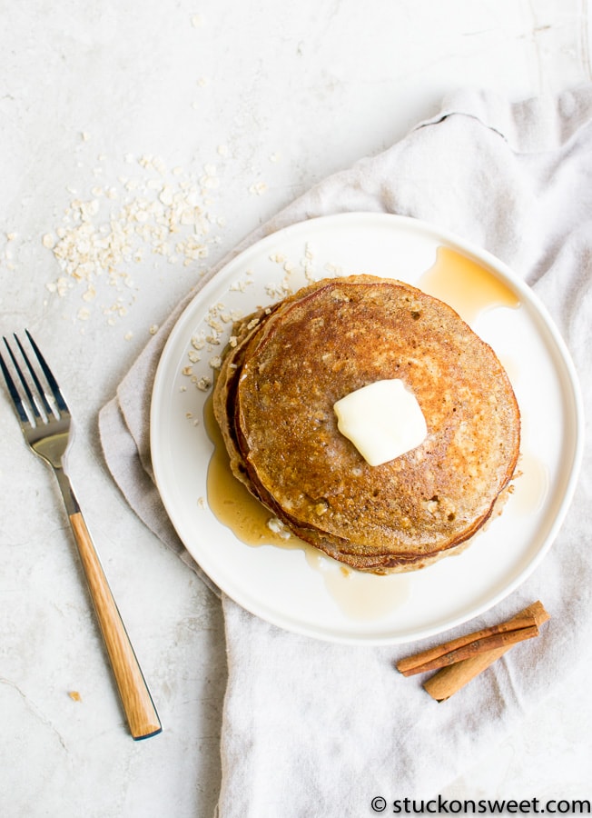 Golden brown homemade pancakes topped with butter and syrup on a white plate. Perfect for breakfast, served with cinnamon sticks and a fork on a rustic background.