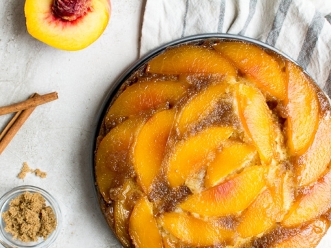 Fresh peach cobbler with caramelized peaches on a rustic white table, served with brown sugar and a striped cloth, highlighting delicious peach desserts, perfect for summer treats.