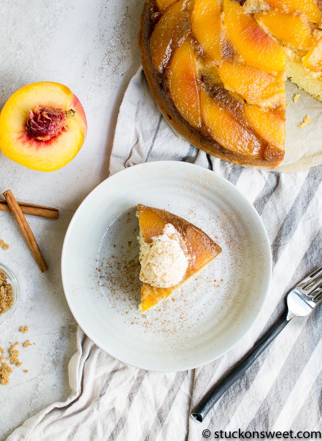 Fresh peach upside-down cake on a white plate with a slice served with vanilla ice cream, cinnamon, and peach halves on the side, perfect for summer desserts.