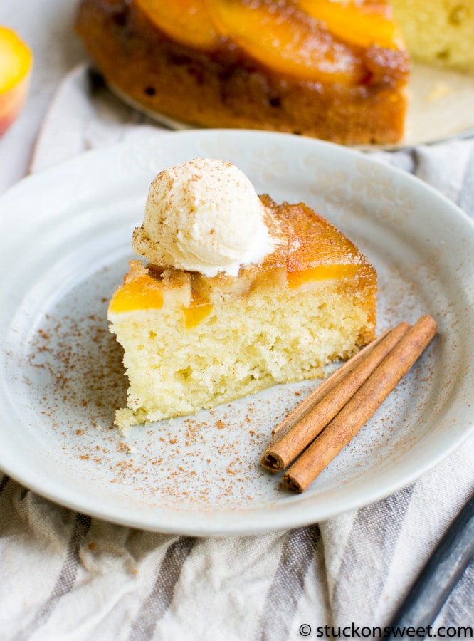 Cream cheese peach cobbler slice topped with whipped cream and cinnamon sticks on a white plate for a sweet dessert.