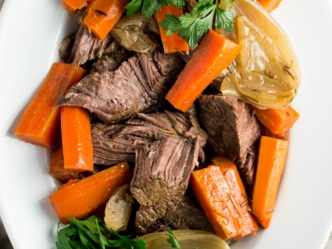 Savory beef stew with carrots, onions, and fresh herbs on a white platter, perfect comfort food.