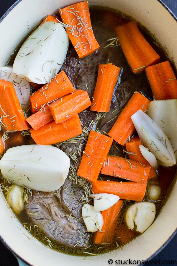 Carrots, onions, and garlic cooking in a savory broth with herbs in a pot.