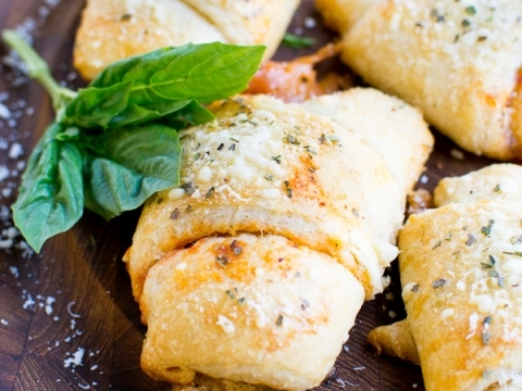 Golden baked stuffed Italian bread rolls with melted cheese and herbs garnished with fresh basil on a rustic wooden serving board.
