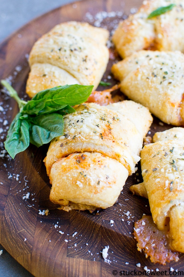 Golden baked stuffed Italian bread rolls with melted cheese and herbs garnished with fresh basil on a rustic wooden serving board.