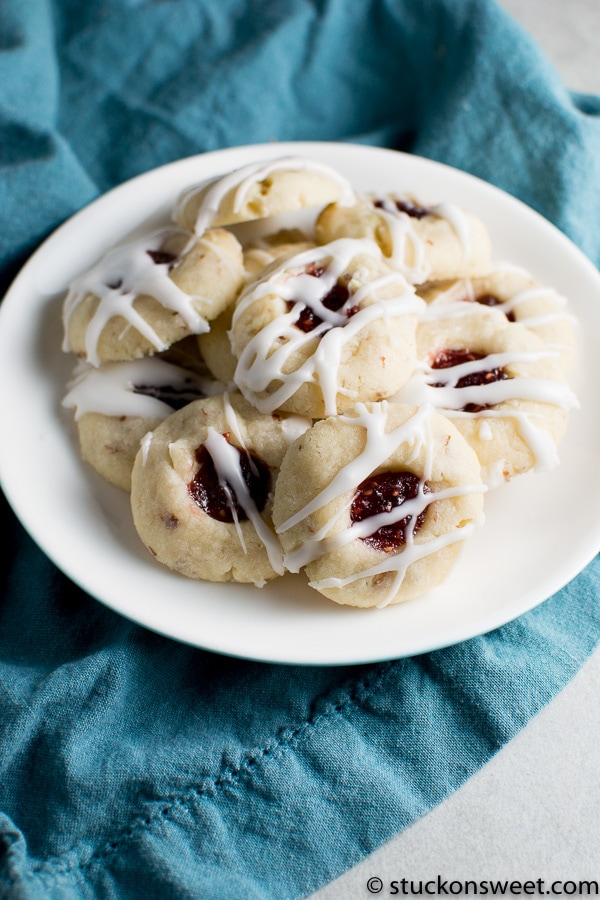 Soft sugar cookies with fruit jam filling drizzled with white icing on a white plate, perfect for dessert or snack.