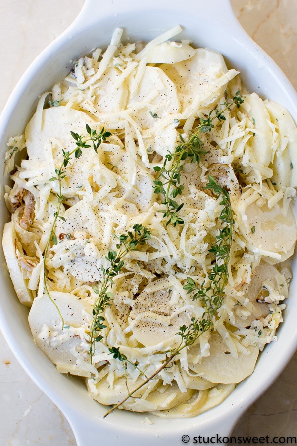 Creamy mashed potatoes topped with shredded cheese and fresh thyme, served in a white baking dish for a comforting and cheesy side dish.