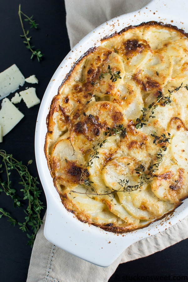 Creamy potato gratin with melted cheese and fresh thyme in a white baking dish.