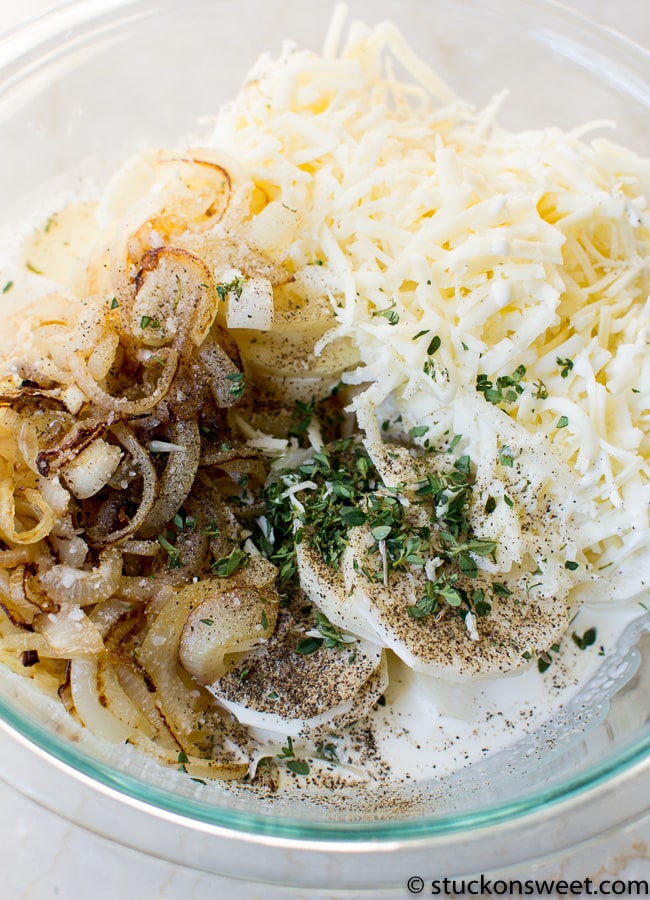 Creamy mashed potatoes with shredded cheese, sautéed onions, and fresh herbs in a glass bowl.