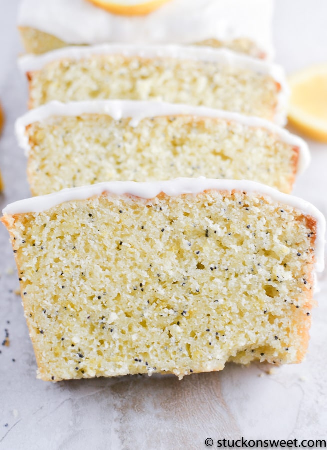 Fluffy lemon cake slices with vanilla icing and poppy seeds on a white surface.