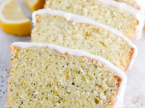 Lemon cake slices with white icing and lemon wedges on top, fresh lemon pieces around, light background.