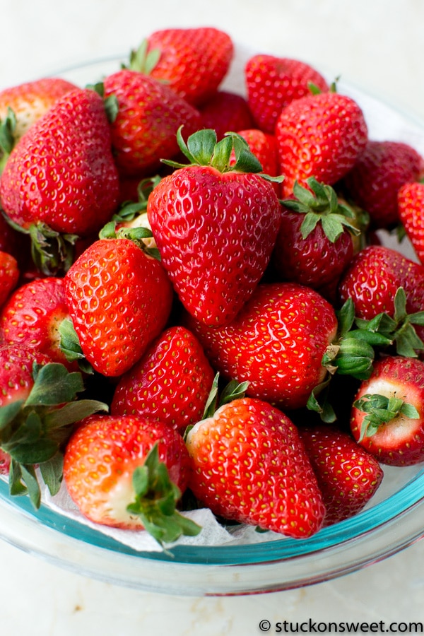 Fresh ripe strawberries with green leaves in glass bowl - perfect for desserts and snacks.