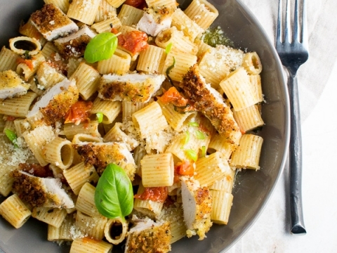 Creamy baked ziti pasta with marinara sauce, mozzarella, and fresh basil on a gray plate.