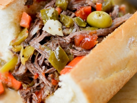 Slow cooker beef pot roast sandwich with shredded beef, green olives, carrots, and bread bun. Perfect hearty meal for comfort food lovers.