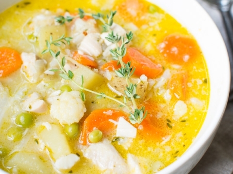 Creamy chicken vegetable soup with carrots, peas, potatoes, and fresh herbs in a white bowl, perfect for comfort food meals and healthy homemade soup recipes.