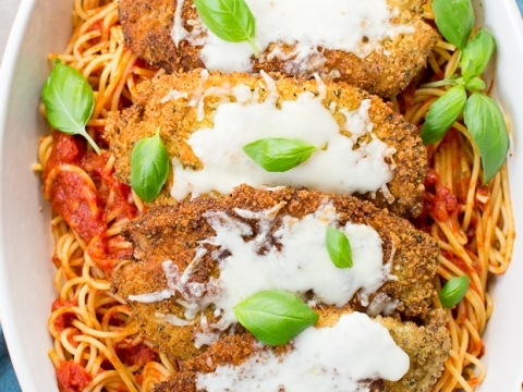 Breaded chicken parmesan over spaghetti with tomato sauce, topped with melted mozzarella and fresh basil leaves.
